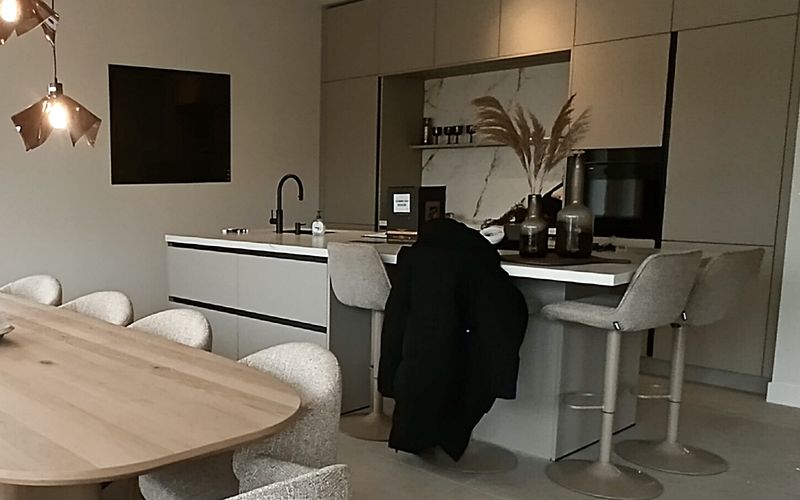 Moderne keuken met kookeiland, hoge beige kasten en een achterwand in marmerlook, met een houten eettafel ervoor